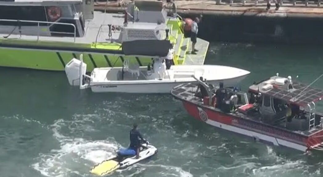 Rescue teams on boats and personal watercraft conduct search operations in Biscayne Bay after a sailboat sinks off Hibiscus Island in Miami Beach, with a rescuer towing a yellow board.